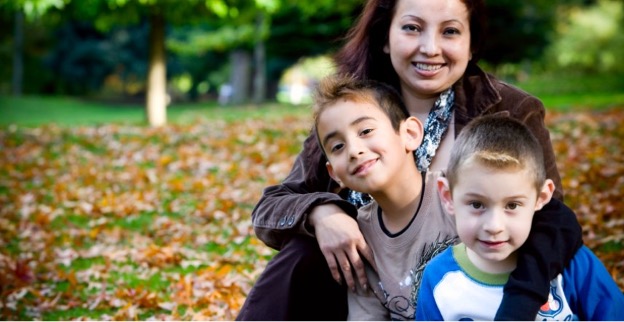 Latina mother and two sons hugging outside on a lawn covered in Autumn leaves