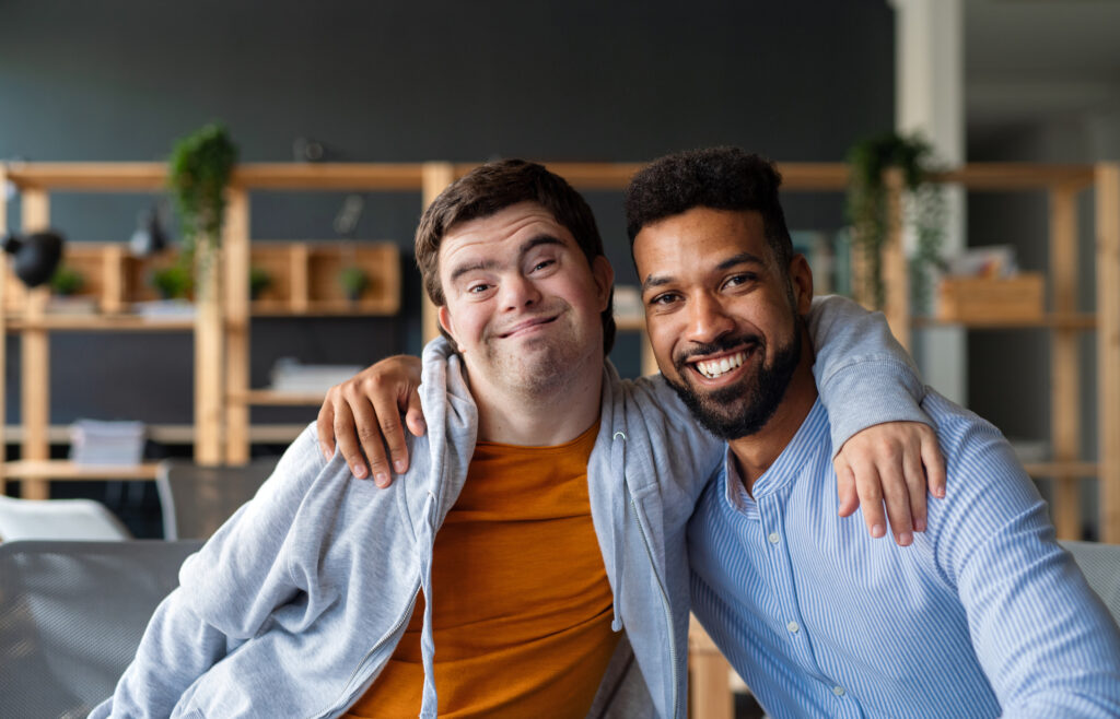 Young white man with Down syndrome and Black man wrap their arms around each other's shoulder