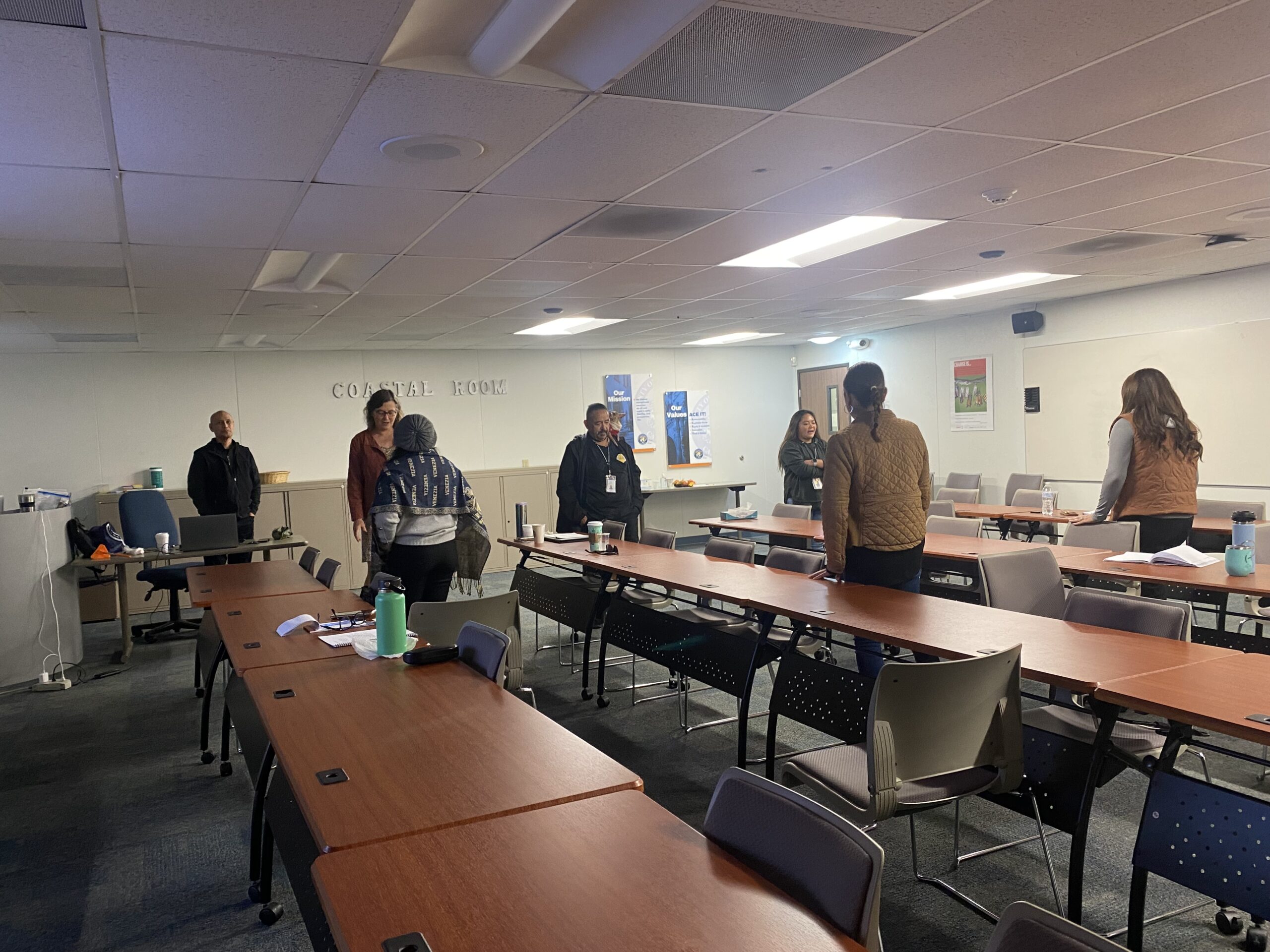 Participants in Painted Brain’s Disability Cultural Competency Development Project pair off for an exercise as they stand between long, brown tables in a brightly lit conference room.